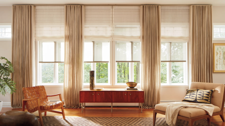 Living room with windows featuring ripple fold drapery in natural Linen layered over desert-hued Sahara Stripe Roman shades.
