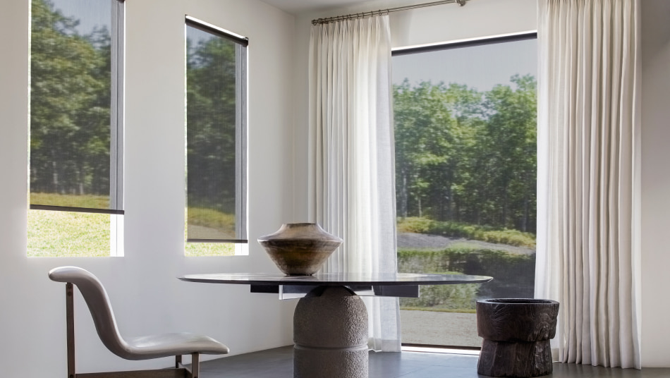 Dining room with windows featuring 10% solar shades in black and Luxe Linen tailored pleat drapery in optic white.