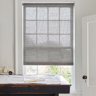 A desk in front of a sunny window with a roller shade in a home office.