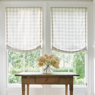 A quaint alcove has a table with flowers and Relaxed Roman Shades made of Holland &amp; Sherry Emerson fabric over the windows.