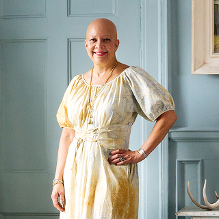 Window treatment designer Sheila Bridges for The Shade Store, wearing a yellow dress against a blue paneled wall.