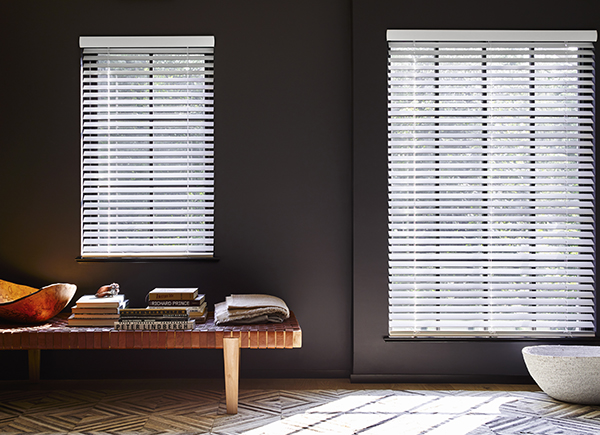 Windows featuring wood blinds in 2 inch matter edge ivory smoke in a room with dark walls and a wood bench with books