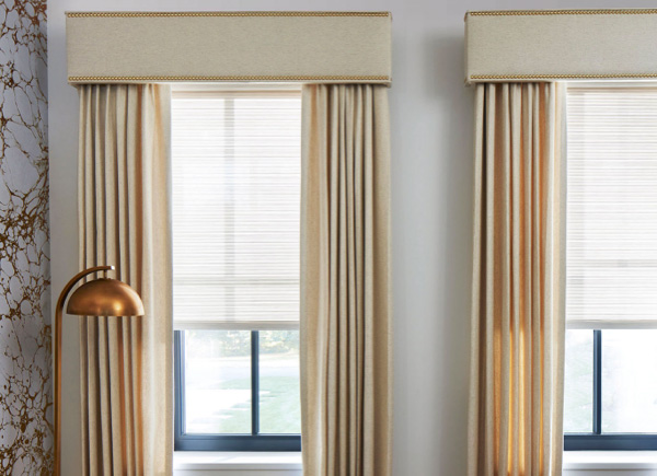 Cornices with Nailheads featured over matching Drapery hung over windows in a room with a marble wall and a gold lamp