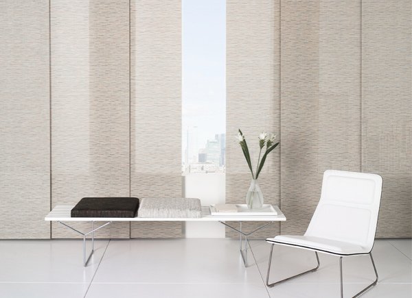 Large windows featuring designer Vertical Blinds in bamboo oat with a city view with a white bench and white chair
