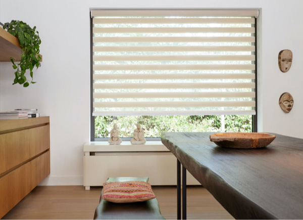 A mid-century modern dining room has a rustic wood table and a window with a Double Roller Shade made of Windansea in Canyon