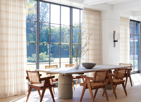 A wall full of windows featuring tailored pleat drapery in a dining room with a large stone table and wooden chairs