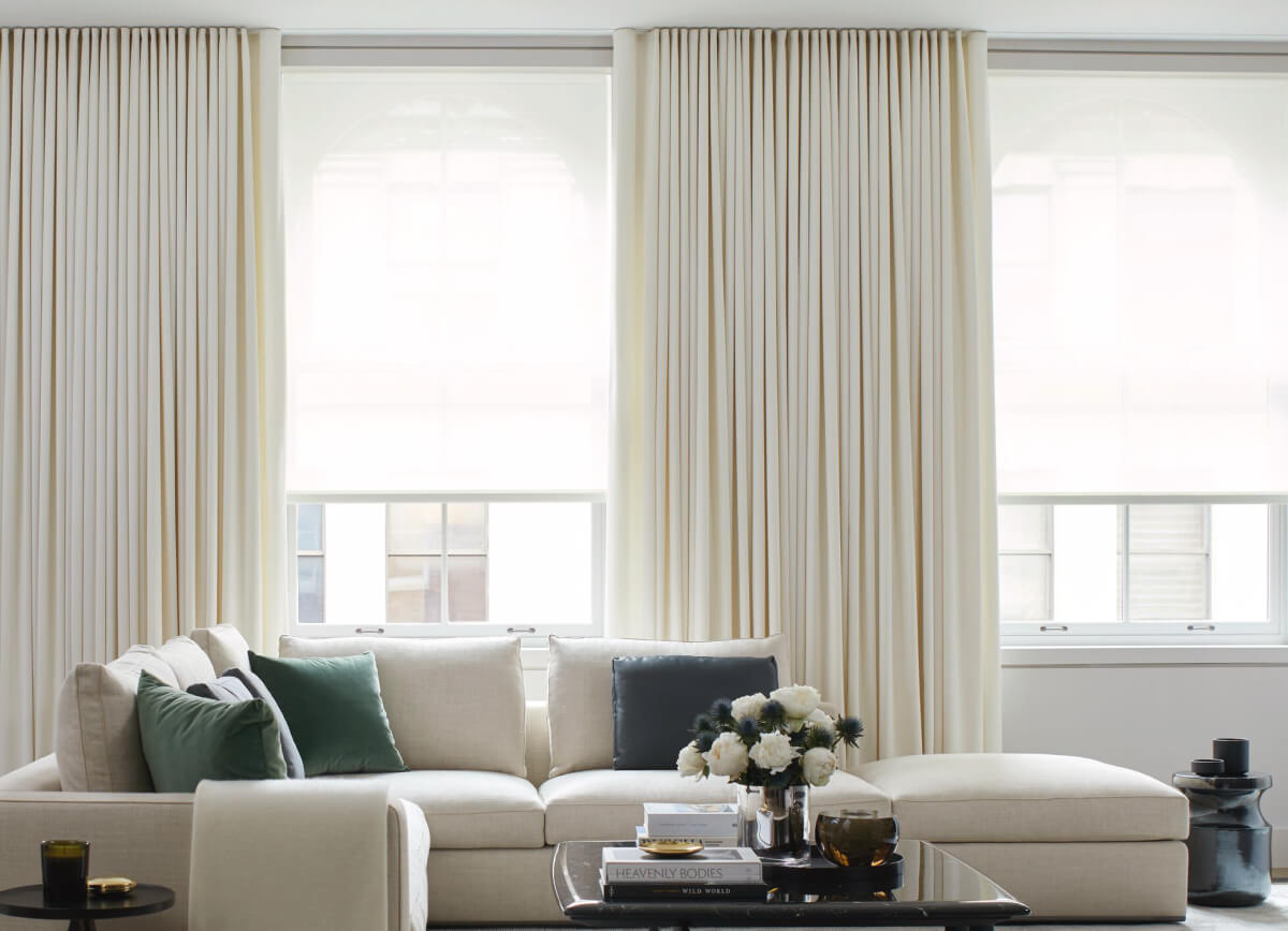 Bright living room with a white sofa and large windows in the background dressed with Energy Efficient Drapery & Solar Shades.