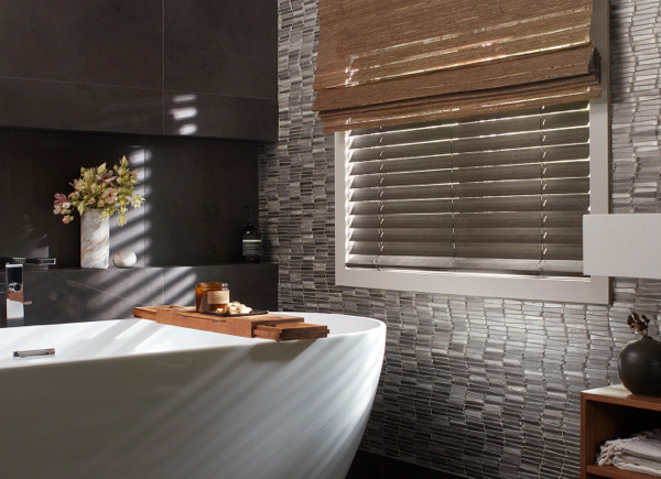 A window featuring faux wood blinds layered under waterfall woven wood shades in a Bathroom with tiled walls and a bathtub A window featuring faux wood blinds layered under waterfall woven wood shades in a Bathroom with tiled walls and a bathtub