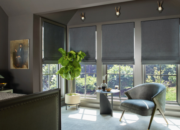 Large windows featuring flat roman shades in wool sateen grey in a bedroom with dark walls and furniture and a tall plantpoh