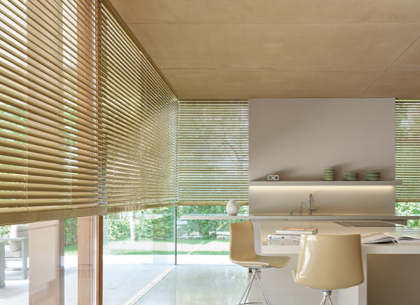 A wall of floor to ceiling windows featuring 2 inch metal blinds in champagne in a kitchen with a large white island 