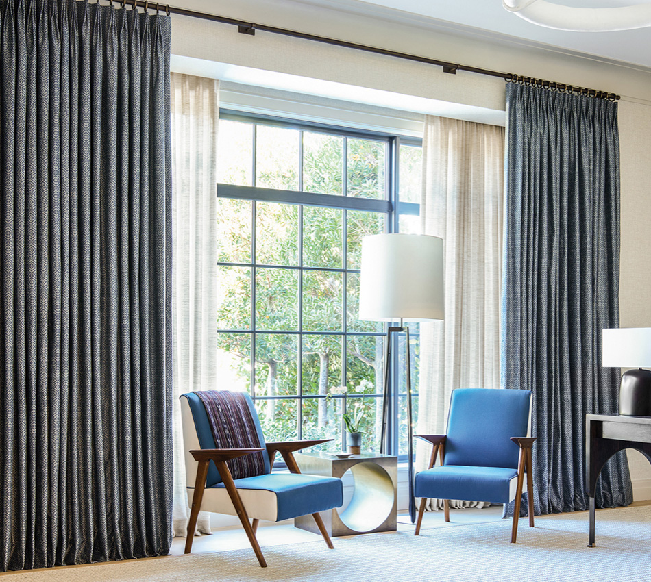 A floor to ceiling window with black panes featuring tailored pleat drapery in two layered fabrics in a living room