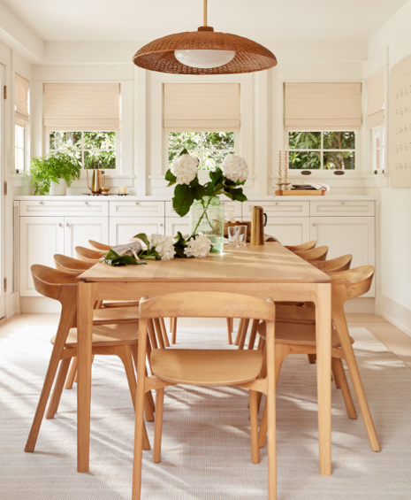 4 windows featuring woven wood shades in a kitchen with white cabinets and a large wooden dining table and matching chairs