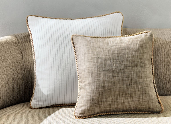 Two square pillows with piping positioned on a neutral couch