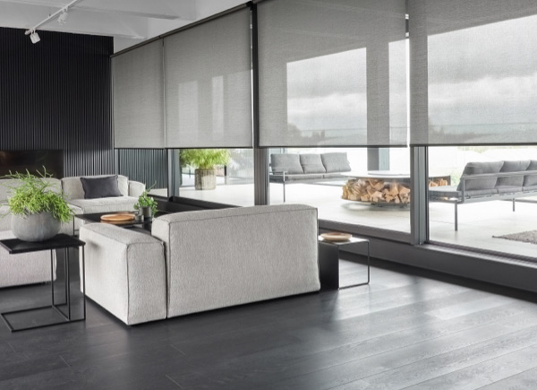 A wall of windows featuring roller shades in 5 percent metallic zinc in a living room with dark walls and grey couches