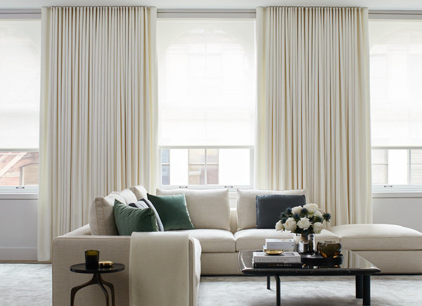 Three windows featuring drapery layered over solar shades in a Living Room with a white couch with blue and green pillows