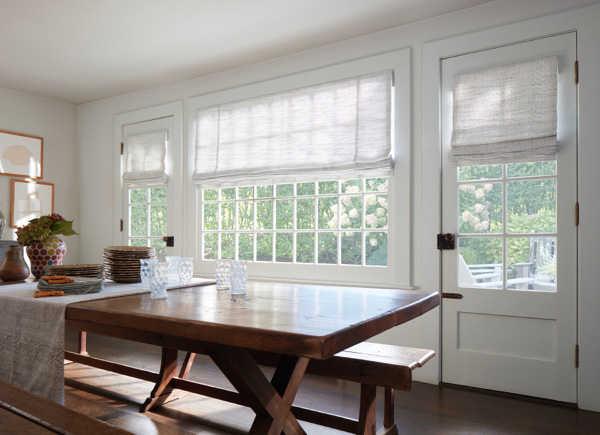 A large centered window and two patio doors featuring roman shades in a Dining Room with a farmhouse style table and benches