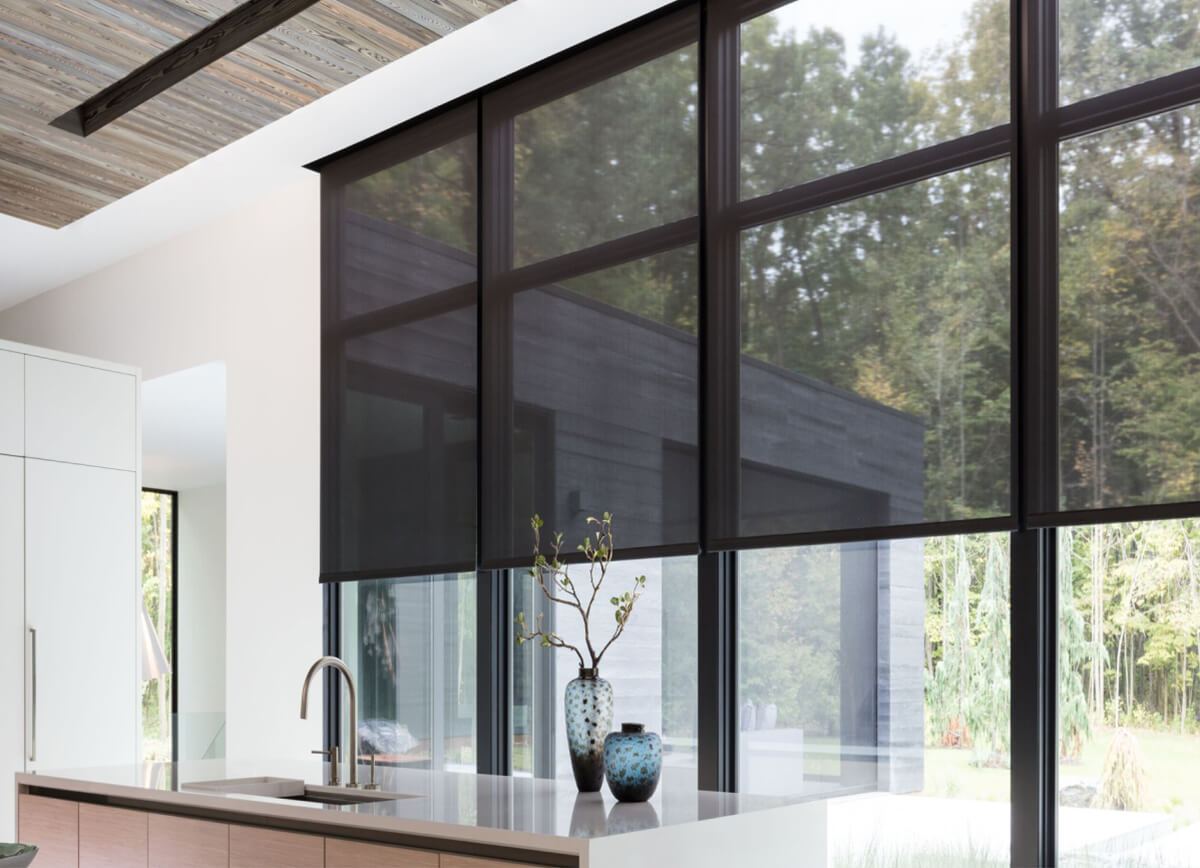 A wall of windows featuring 10% black solar shades in a modern kitchen with an open floor plan overlooking a lush backyard