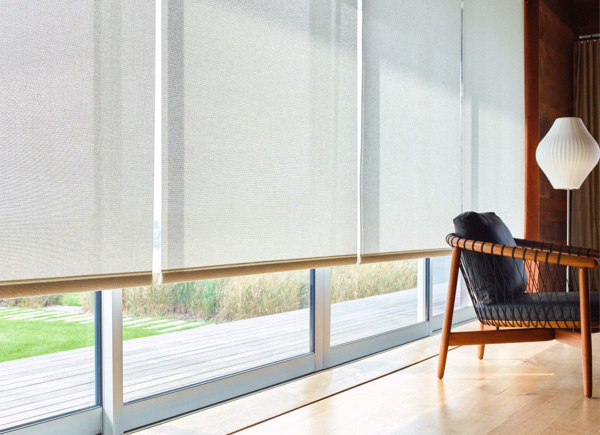 Floor-to-ceiling windows have Solar Shades made of Sunbrella 10% Solistco in Oatmeal, next to wood chair with black cushions