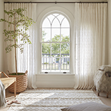 Large arched window with Tailored Pleat Drapery in Feather Palm Embroidery/Vinatge Lace with a tall plant in front of window