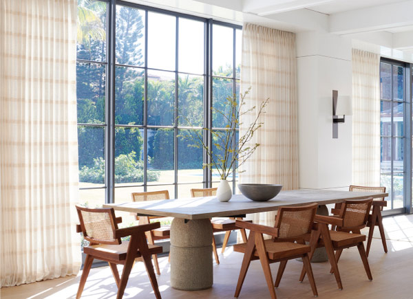 Floor to ceiling windows featuring Tailored Pleat Drapery in Lily Buff in a dining room with a stone table and wood chairs Floor to ceiling windows featuring Tailored Pleat Drapery in Lily Buff in a dining room with a stone table and wood chairs