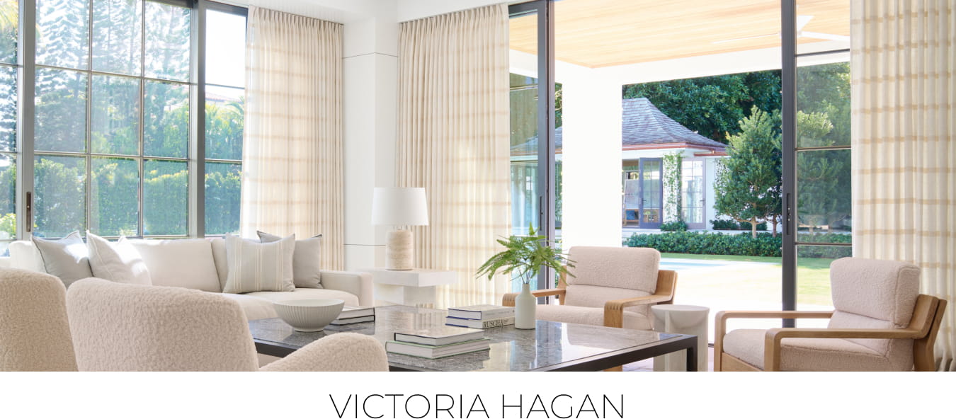 Corner of a bright, airy living room with windows featuring Tailored Pleat Drapery in Victoria Hagan's Lily fabric in Buff.