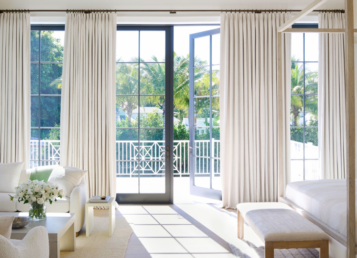 A bright and airy bedroom with floor-to-ceiling Tailored Pleat Drapery in Petal Pearl hung over large patio doors