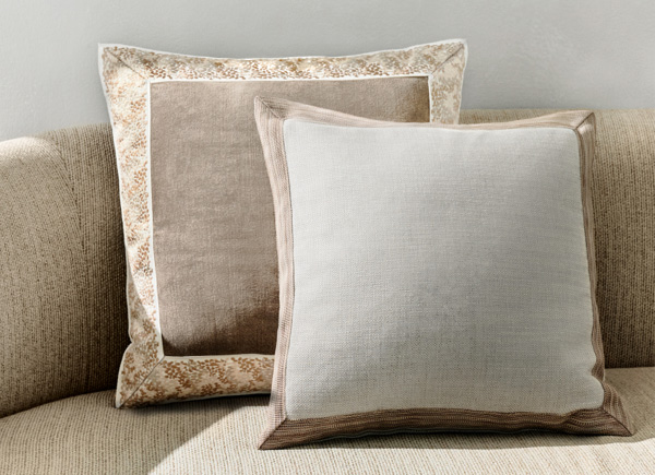Two square pillows with tape borders positioned on a neutral couch