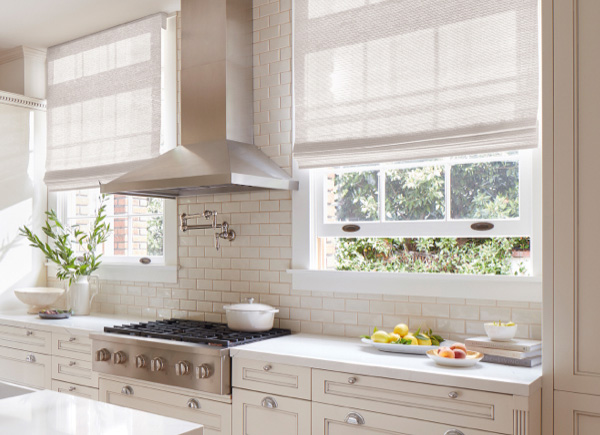 Two windows featuring Waterfall Woven Wood Shades in Monterey White in a kitchen with white cabinets and a white tiled wall