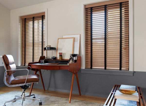 Two windows featuring wood blinds in 2 inch oak on either side of a wooden desk in an office with grey and white walls