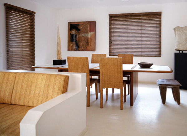 Two windows featuring wood blinds in a Dining Room with a wooden table and a white couch with brown cushion and brown decor