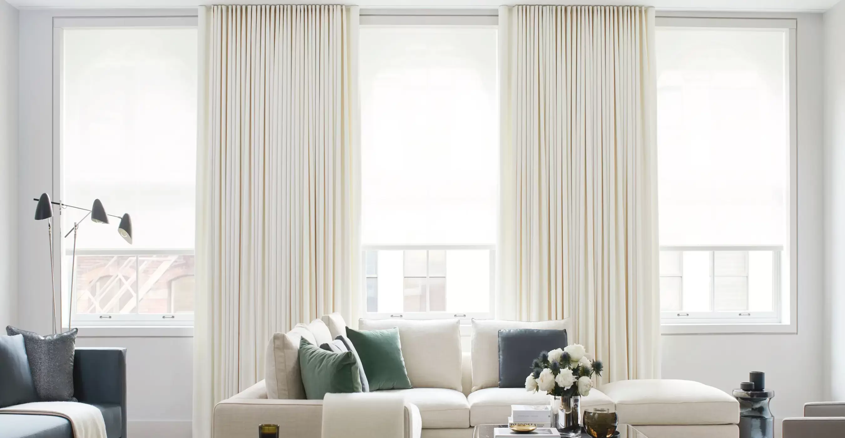 Bright living room with a white sofa and large windows in the background dressed with Energy Efficient Drapery & Solar Shades