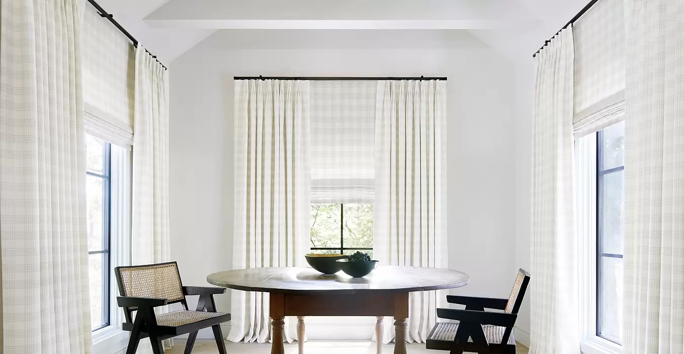 A dining room with windows on all 3 walls. Roman Shades paired with Pinch Pleat drapery in Holland & Sherry Emerson fabric