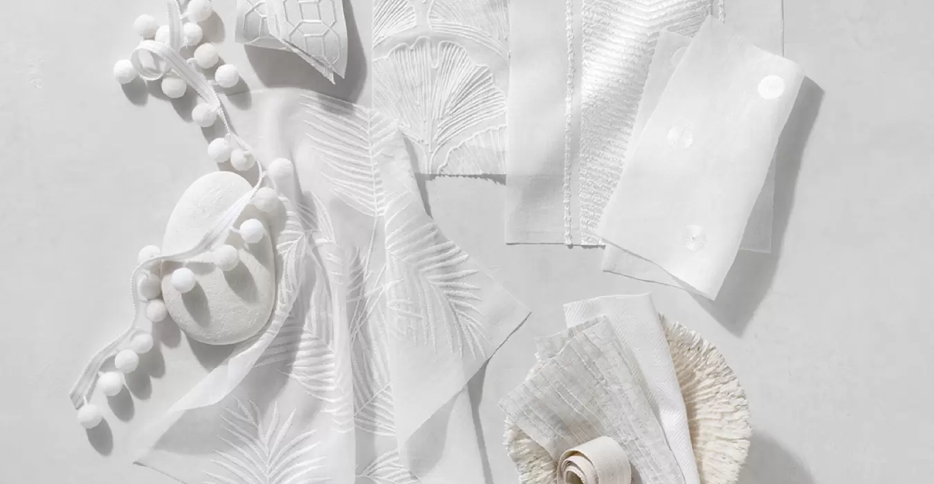 White fabric swatches like Palmier, Feather Palm Embroidery, Nomad Stripe & more lay decoratively on a white table