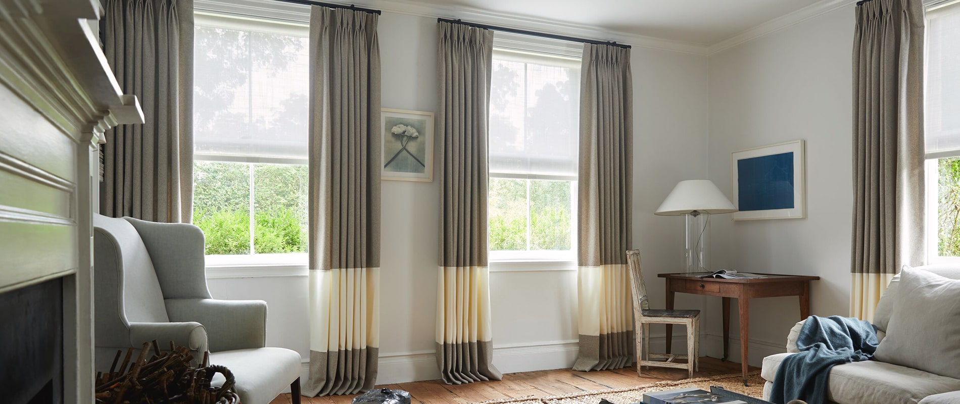 Cozy sitting room with wool blend pinch pleat drapery in flax and snow layered over Naomi roller shades in seashell.