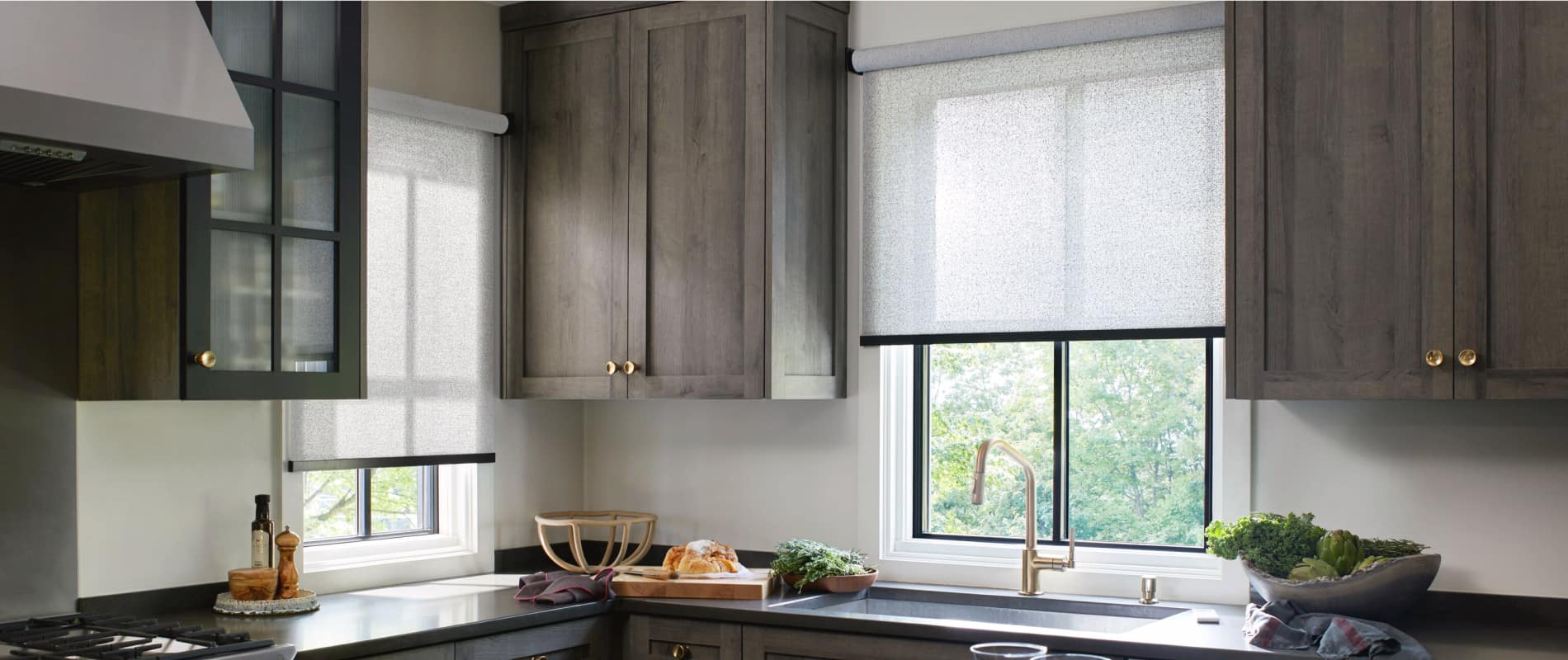 Corner of a sleek, modern kitchen with two windows featuring 3% Solistico Sunbrella roller shades in an ash-gray hue.