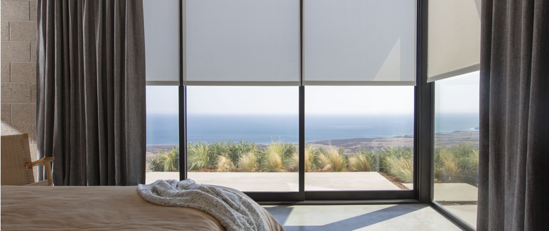 Corner wall of floor to ceiling windows featuring Roller Shades 5% Metallic in Copper in a bedroom with beach views