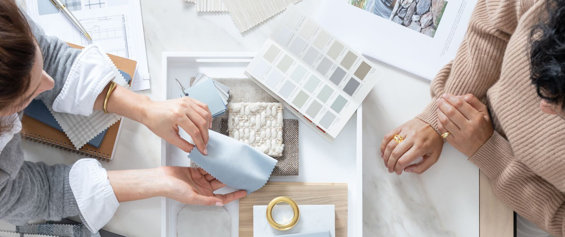 Two women sit at a table reviewing fabric swatches and The Shade Store Lookbook during a design consult appointment.