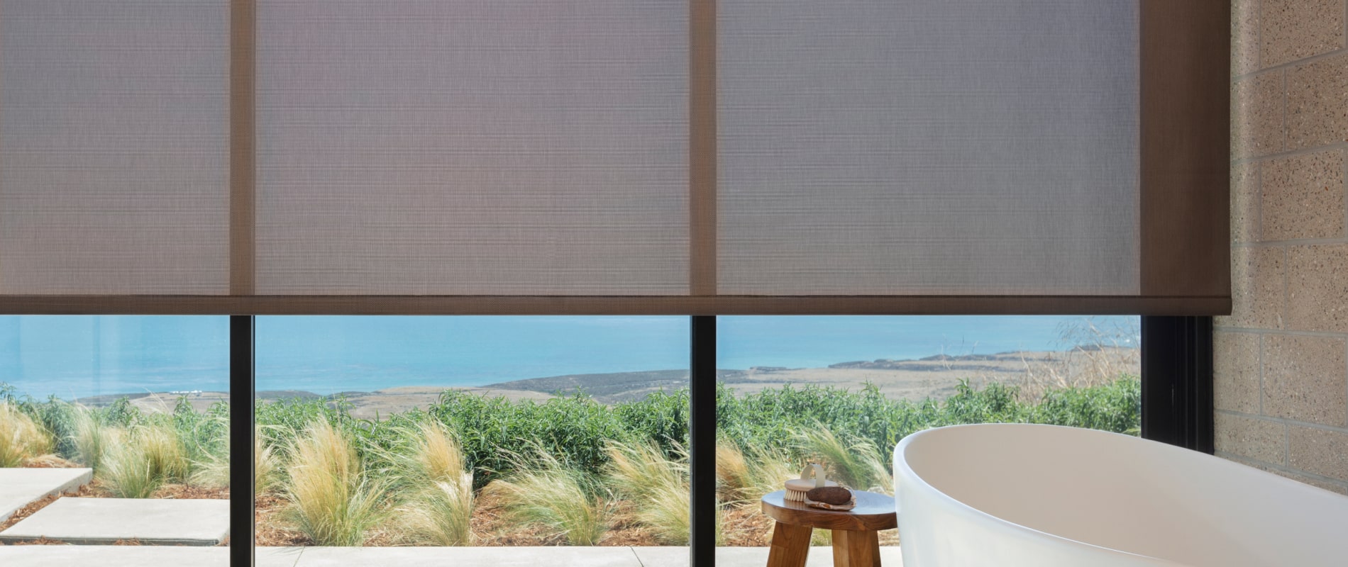 Corner of bathroom with floor-to-ceiling windows and beach views featuring 5% Metallic roller shades in a Copper hue.