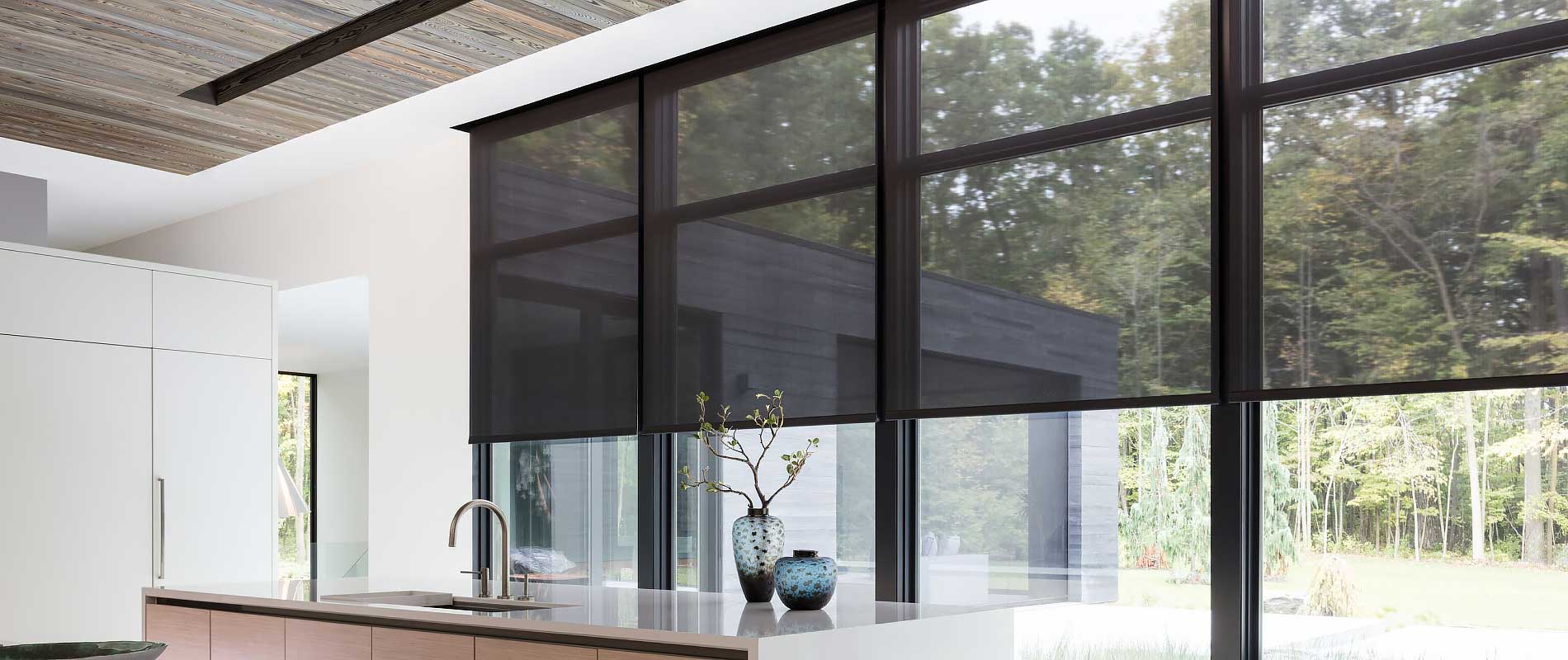 A wall of windows featuring 10% black solar shades in a modern kitchen with an open floor plan overlooking a lush backyard