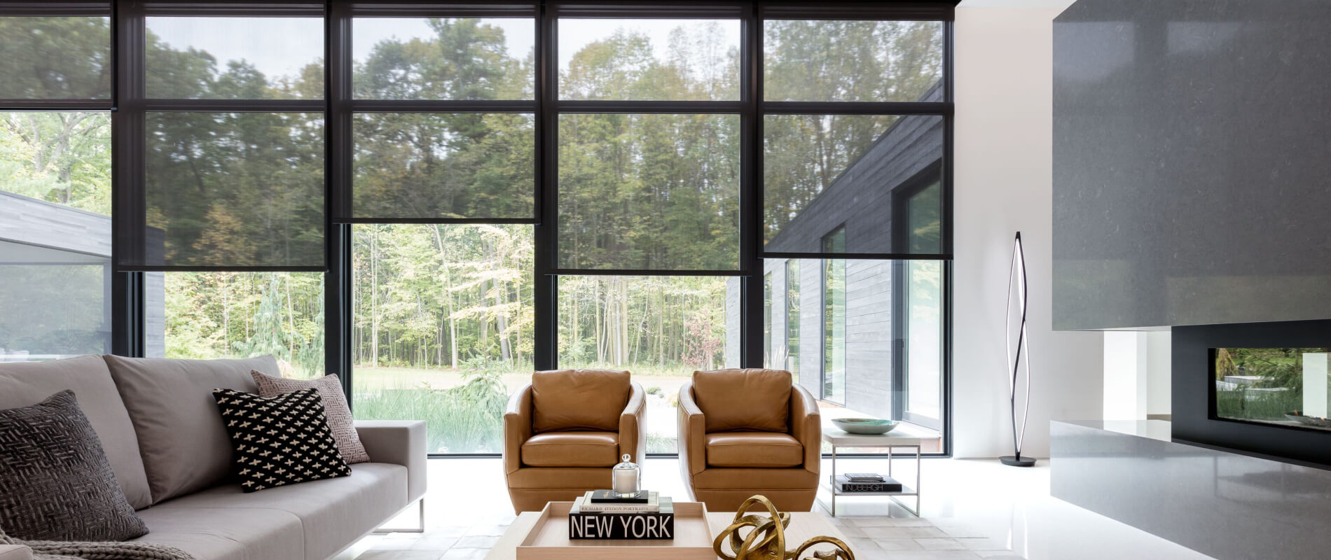 Spacious living room with a gray couch and a modern fireplace with large wall of windows dressed with 10% black solar shades