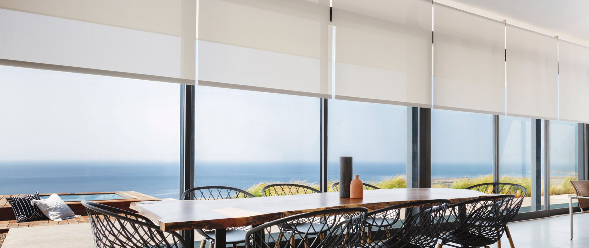 Full wall of windows in a large dining room with beach views featuring solar shades in 5% Grey fabric.