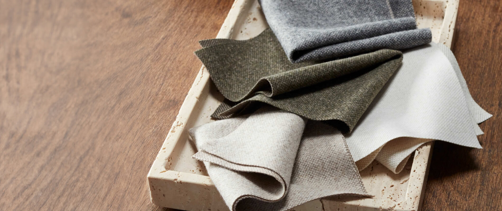 A selection of four lowell tweed swatches by Nate Berkus in a small white tray on top of a dark wood surface