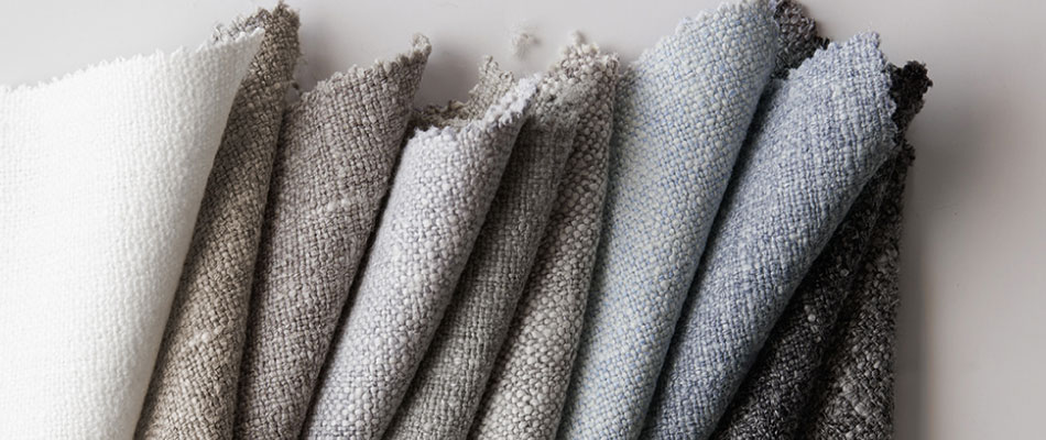 Swatches of Heathered Linen in neutral colors are folded on a plain white table to showcase the texture of the swatches