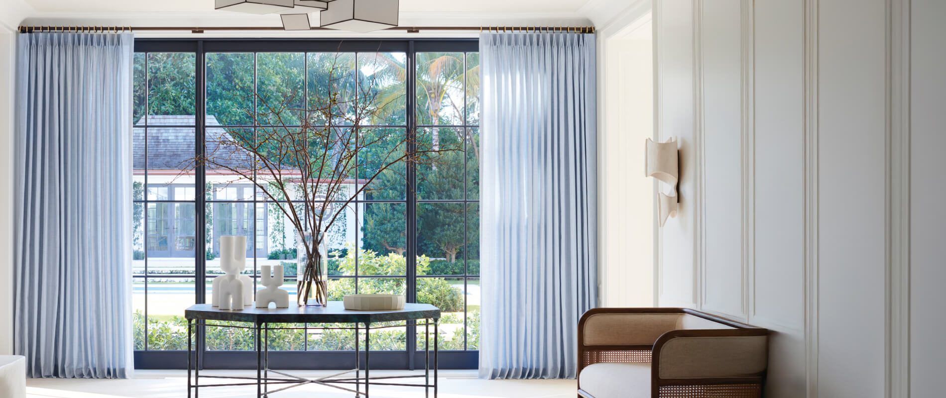 A bright reception room with a table and a large plant in front of paned windows with Tailored Pleat Drapery in Casa Stripe.