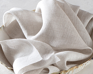 A luxe sheer linen bunched up in a bowl on a stark white tabletop features a soft texture and off-white color