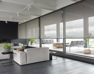 Floor to ceiling windows featuring light filtering roller shades in a grey living room with two couches with promo text