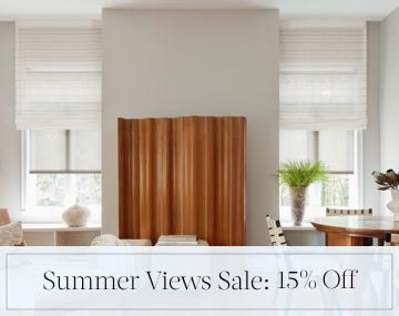 Motorized Roman and Roller Shades hang in a family room with wood decor with sales messaging for Summer Views Sale: 15% Off