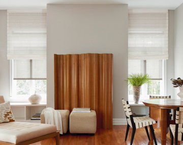 Two tall windows featuring layered motorized roller shades in a dining room with various seating & large centered brown art