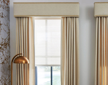 Cornices with Nailheads featured over matching Drapery hung over windows in a room with marble wall and lamp