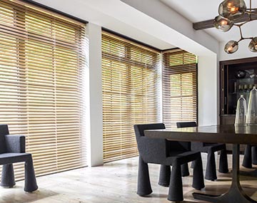 Floor to ceiling windows featuring 2 inch metal blinds in champagne hung in a dining room with a dark table and black chairs
